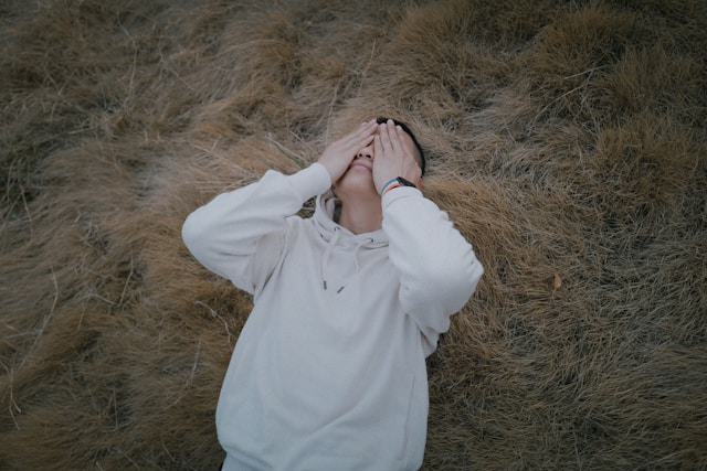Young man covering face in grass overwhelmed by depression and stress