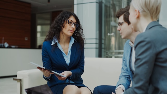 Professional woman talking with two adults during a meeting in a modern office lobby.