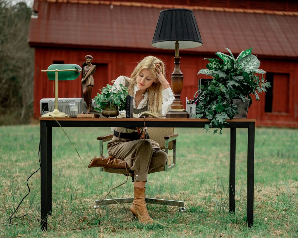 Woman sitting at a desk outdoors with her head resting on her hand.