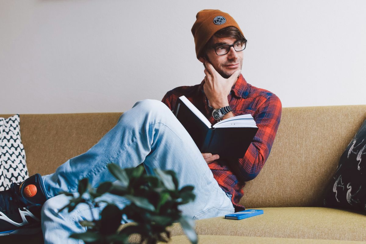 Man sitting on a couch holding a notebook and looking thoughtful.