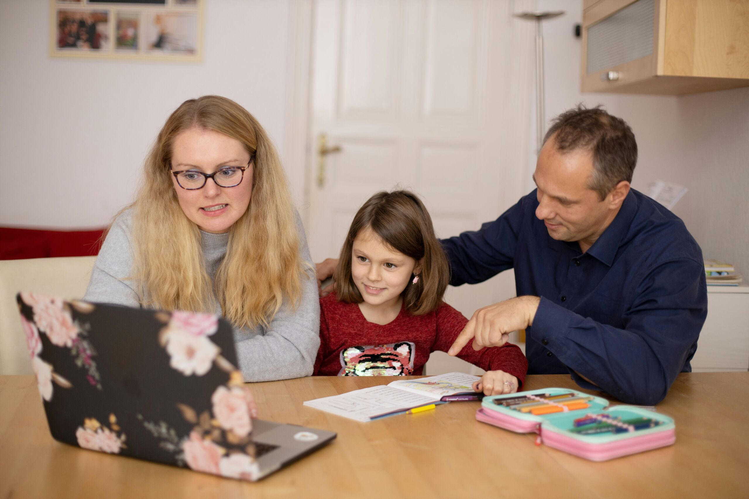 Two parents and a child sitting at a table looking at a laptop and school materials