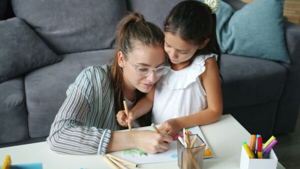 Adult and child sitting together at a table drawing with colored pencils