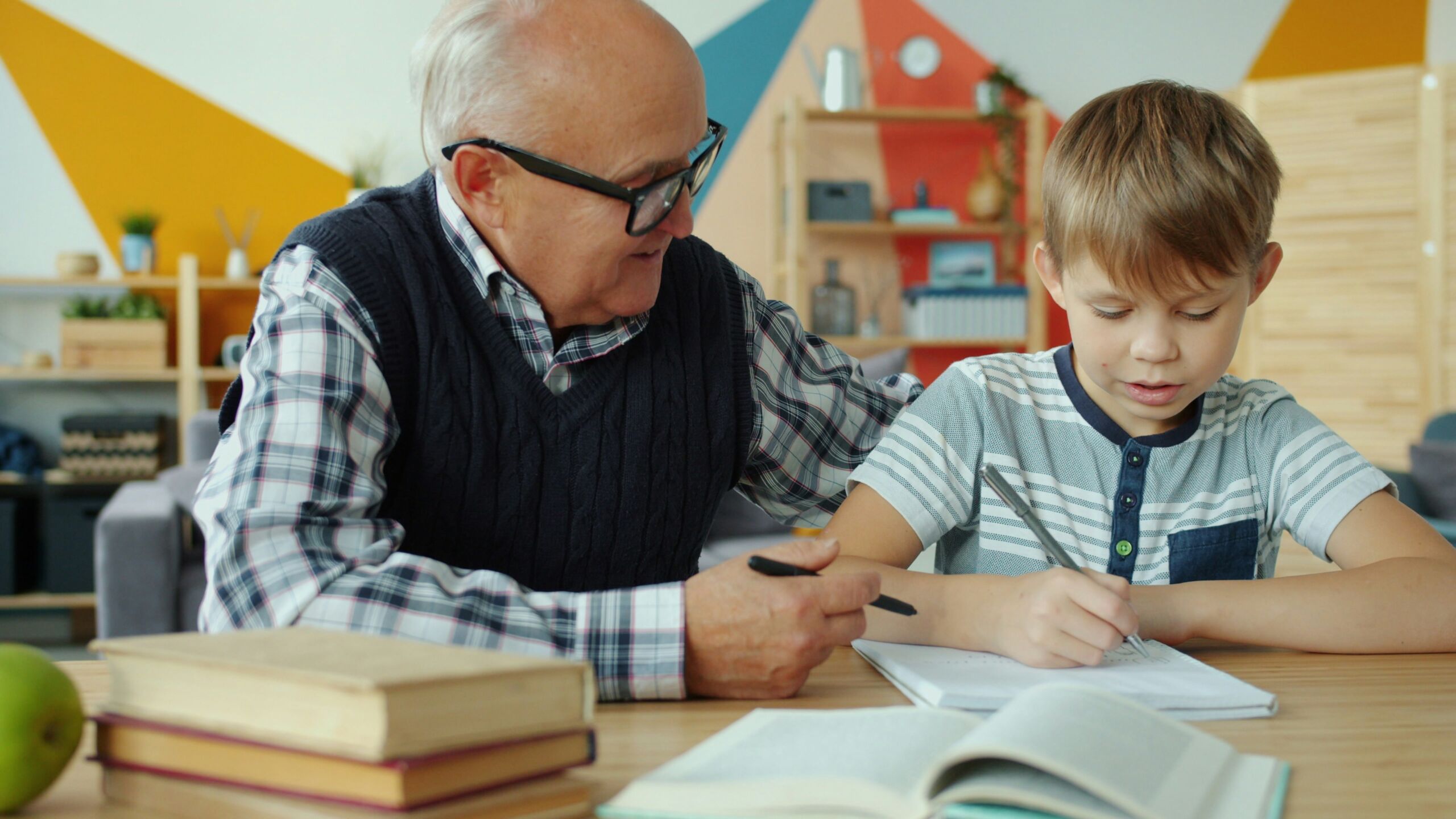 Older adult sitting beside a child and offering guidance while the child writes in a notebook